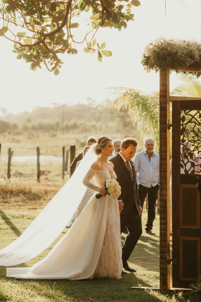 Mariée accompagnée par son père avançant dans l'allée de la cérémonie dans un jardin.